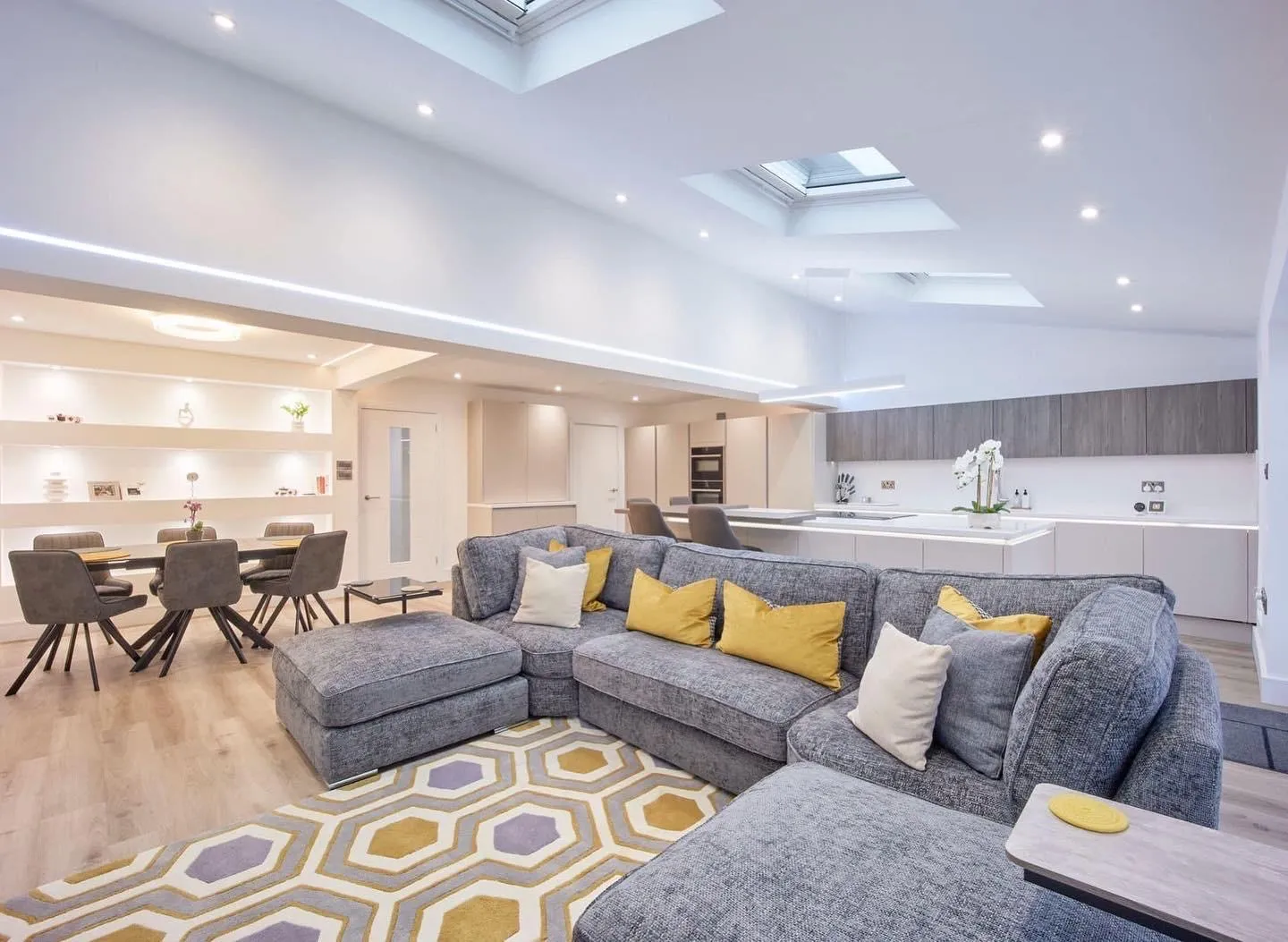 An open-plan living, dining and kitchen extension under rooflights, with LED strip lighting built into the ceiling beam.